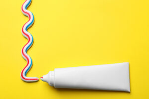 Blank tube with squeezed out toothpaste on yellow background, flat lay. Space for text