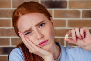 redhaired ginger female with pain grimace holding white wisdom tooth after surgery removal extracted of a tooth